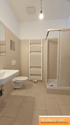 Badezimmer mit Dusche, Toilette, Handwaschbecken und Waschmaschinenanschluss